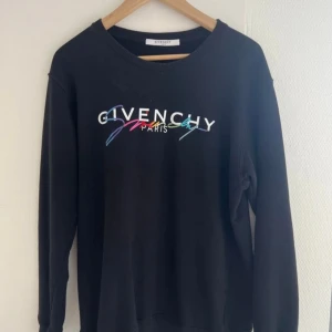 Blå tröja från Givenchy - Säljer en snygg svart tröja från Givenchy i storlek M. Tröjan är i 100% bomull och har ett färgglatt broderat Givenchy Paris-märke på framsidan. Perfekt för både vardag och fest! 🖤