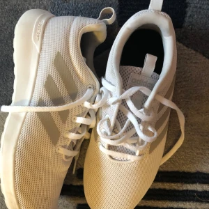 Vita sneakers från Adidas - Säljer ett par vita Adidas sneakers i mycket bra skick. De har en stilren design med de klassiska tre ränderna på sidan. Skorna är i syntetmaterial med snörning och en bekväm sula, perfekta för både vardag och träning. Passar till det mesta och är superbekväma!