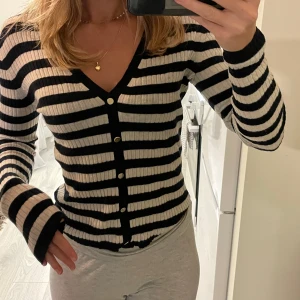 Randig tröja från Filippa K - Säljer en snygg och stilren randig kofta från Filippa K. Den är svart och vit med knappar hela vägen ner och har en v-ringad design. Perfekt för både vardag och lite finare tillfällen. Koftan är i bra skick och passar perfekt till höst och vår. Väldigt skönt material! Aningen ”urtvättad”. 