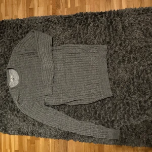 Grå kabelstickad tröja - Säljer en stilren grå ribbad tröja i mycket bra skick. Perfekt för kyliga höst- och vinterdagar. Tröjan har långa ärmar och en bekväm passform som passar till det mesta. Ett måste i garderoben för den som gillar enkel och snygg design.