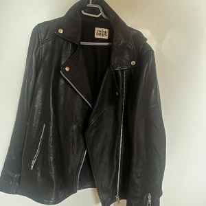 Svart skinnjacka från Twist & Tango - Snygg svart skinnjacka från Twist & Tango i mycket bra skick. Den har en klassisk bikerstil med dragkedjor och knappar i silver. Perfekt för höst och vår, och funkar lika bra till vardags som till fest. Jackan har en normal passform och långa ärmar.