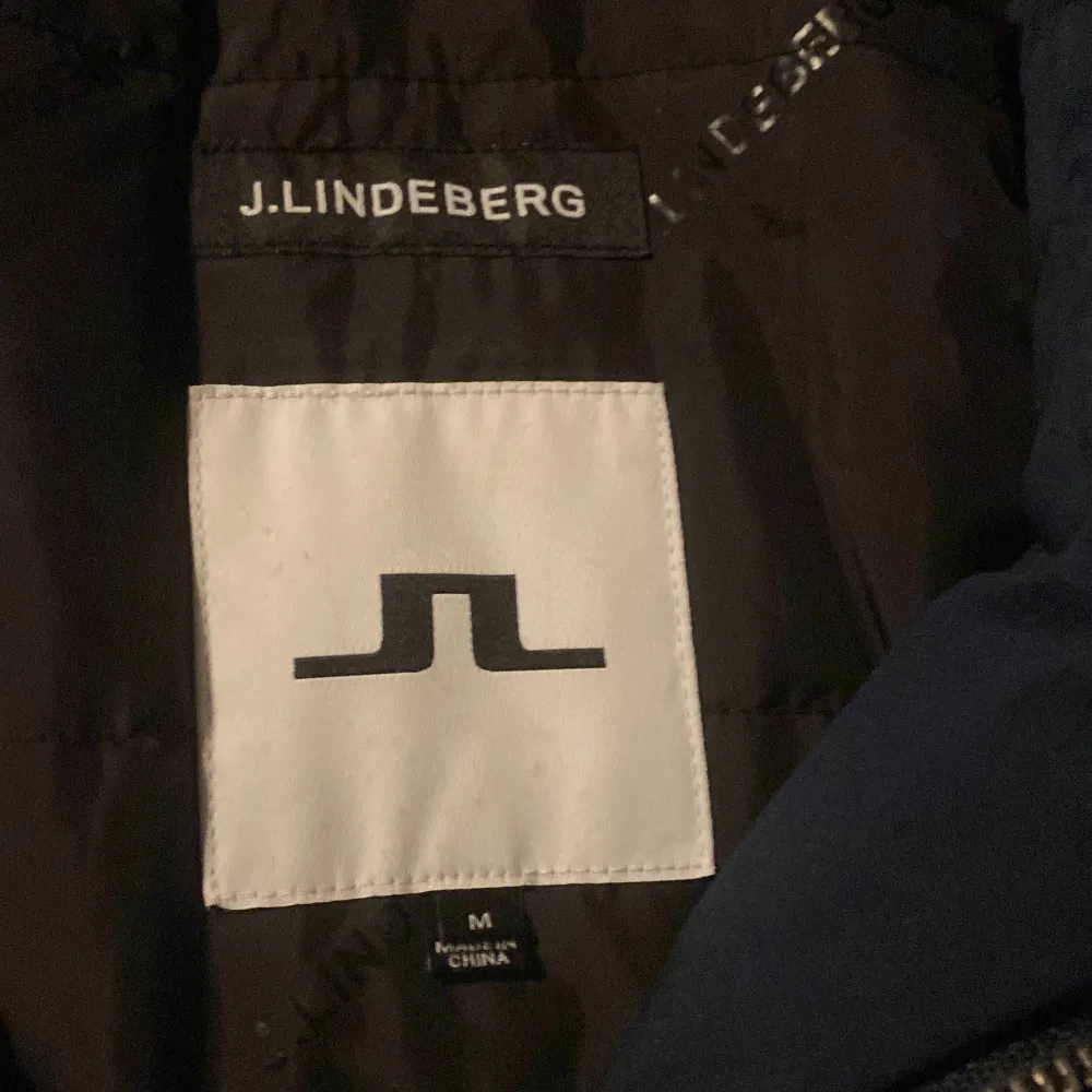 Säljer en snygg mörkblå jacka från J.Lindeberg i storlek M. Jackan har en stilren design med dragkedja och knappar framtill. Perfekt för höst och vinter med sin quiltade insida som håller dig varm. Den har flera praktiska fickor och är i mycket bra skick. Passar både till vardags och lite finare tillfällen.. Jackor.