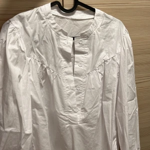 Vit henley-skjorta stl L - Säljer en stilren vit skjorta. Skjortan har en avslappnad passform med långa ärmar och knappar framtill. Har aldrig fått tid att använda den då jag redan har för många skjortor hehe