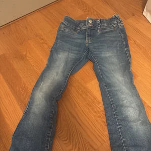Blå bootcut jeans från H&M - Säljer ett par snygga blå bootcut jeans från H&M i storlek 158. De har en justerbar midja och är lågmidjade, vilket ger en skön passform. Perfekta för vardagsbruk eller en avslappnad dag ute. De är i bra skick och redo för en ny ägare!