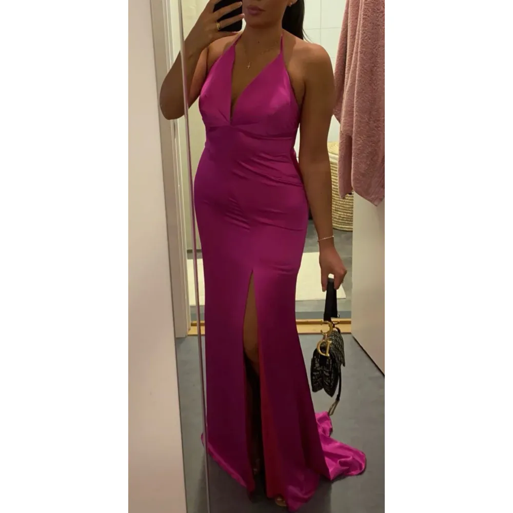 Säljer en fantastisk rosa långklänning i satin med en elegant slits framtill. Klänningen har en djup v-ringning och är ärmlös, perfekt för festliga tillfällen. Den sitter tight och framhäver figuren på ett smickrande sätt. Perfekt för bröllop och förlovning eller andra speciella tillfällen!. Mekot.
