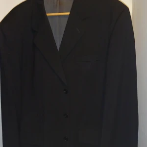 Svart kavaj från Hampton Republic - Snygg svart kavaj från Hampton Republic i klassisk stil. Perfekt för både formella och semi-formella tillfällen. Kavajen har en enkel knäppning och en stilren passform. Passar utmärkt till både vardag och fest.