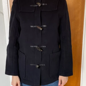 Gloverall duffel med luva - Klassisk Gloverall navy blå duffelkappa med luva. 80% ull. Mycket fint skick. Inga defekter. Strlk 36.