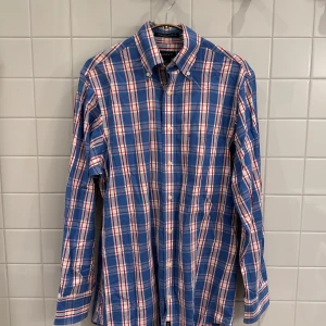 Rutig skjorta från GANT i blå, vit och röd – Storlek S - Superfin rutig skjorta från GANT i färgerna blå, vit och röd, i storlek S. Det finns ett litet hål under kragen, men det syns inte när skjortan är på tack vare button-down modellen. Se sista två bilderna för detaljer.