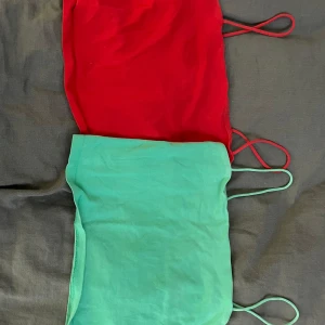 Två tubtoppar i rött och grönt - Säljer två snygga tubtoppar i rött och grönt. Perfekta för sommaren eller en festlig kväll. De är axelbandslösa och har en enkel design som gör dem lätta att matcha med olika outfits. Passar bra till både jeans och kjol!