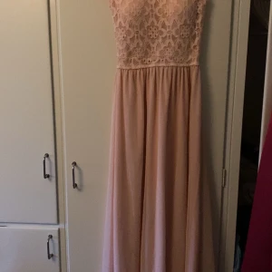 Ljusrosa spetsklänning - Säljer en superfin ljusrosa långklänning med spetsdetaljer. Perfekt för sommarens fester eller kanske en bal. Klänningen är ärmlös och har en vacker spetsdesign upptill som ger en romantisk känsla. Den är i nyskick och passar perfekt för en elegant look.