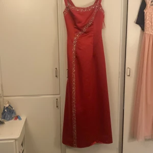 Rosa balklänning med pärldetaljer - Säljer en elegant rosa långklänning med vackra pärldetaljer längs axelbanden och diagonalt över klänningen. Perfekt för festliga tillfällen. Klänningen har en smickrande passform och är tillverkad i ett glansigt material som ger en lyxig känsla.