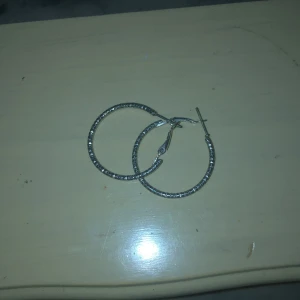 Silvriga hoop-örhängen - Säljer ett par stilrena silvriga hoop-örhängen. De är i nyskick och perfekta för både vardag och fest. Örhängena har en enkel och elegant design som passar till alla outfits. Perfekt accessoar för att ge din look det där lilla extra! ✨
