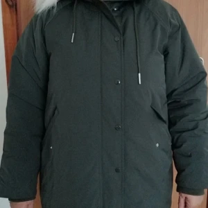 Grön parkajacka från Filippa K - Säljer en snygg grön parkajacka från Filippa K i storlek 40. Jackan har en mysig huva med pälsdetaljer och knäppning framtill. Perfekt för kalla vinterdagar och höstpromenader. Den är i bra skick och redo för nya äventyr!