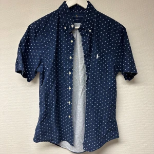 Mörkblå kortärmad skjorta från Ralph Lauren - Stiöig mörkblå skjorta från Ralph Lauren med vitt mönster. Skjortan är kortärmad och har en slim fit passform. Endast använd vid något enstaka tillfälle så nyskick. Strl: M. 