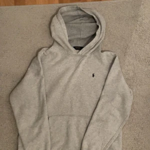 Grå hoodie från Polo Ralph Lauren - Säljer en stilren grå hoodie från Polo Ralph Lauren. Den har en klassisk design med en liten broderad logga på bröstet. Perfekt för både vardag och chill. Den är i bra skick och superbekväm att ha på sig. Passar perfekt till jeans eller joggers!