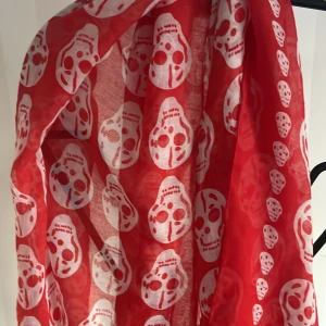 Röd halsduk med dödskallemönster - Säljer en cool röd halsduk med vita dödskallar. Perfekt för att ge din outfit en edgy touch. Den är lätt och passar bra för både höst och vår. Skicket är toppen, nästan som ny!