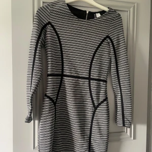 Randig klänning från Divided - Säljer en superfin randig klänning från Divided i storlek S. Den har en snygg svart och vit randig design med svarta detaljer som ger en cool kontrast. Klänningen är figurnära och har trekvartsärmar, perfekt för både vardag och fest. Den har en dragkedja i ryggen för enkel påklädning.