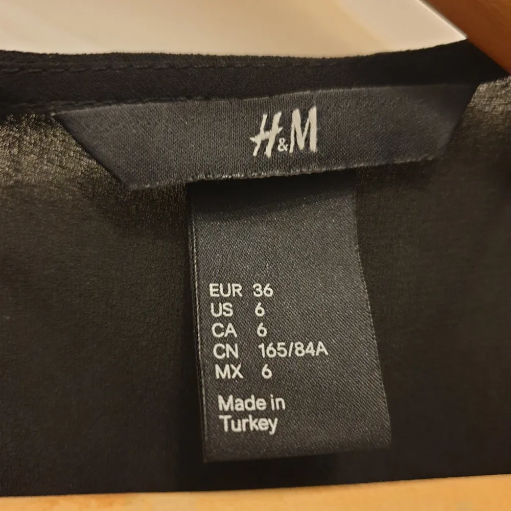 Säljer en Ny, snygg svart topp från H&M i storlek S. Toppen har korta ärmar och är dekorerad med coola nitar längs ärmarna och nederkanten. Perfekt för en kväll ute eller en avslappnad dag med stil.. Toppar.