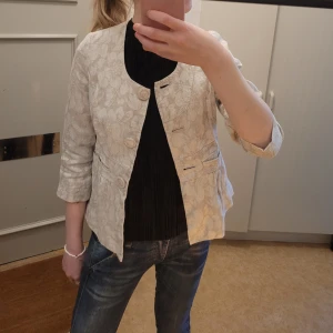 Beige kofta - Beige kofta/jacka med blommigt mönster! Så söt och passar bra att ha som kofta innomhus eller som en jacka på varmara höstdagar! Sällan använd så riktigt bra skick! Skriv vid frågor