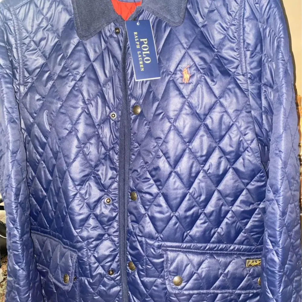 Säljer en snygg blå quiltad jacka från Polo Ralph Lauren. Jackan har en klassisk krage och knappar framtill. Den är perfekt för höst och vår med sin stilrena design och bekväma passform. Den har också praktiska fickor med knappar.. Jackor.