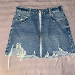Jeanskjol med slitningar och dragkedja - Säljer en cool jeanskjol med slitningar och en framträdande dragkedja framtill. Kjolen är enbart testad möjligtvis använd en gång. Den har också praktiska fickor både fram och bak. Jag tvättar såklart alla kläder innan (om inte nya med lapp) 