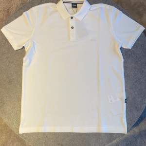 Vit Hugo Boss piké  - Säljer en helt ny och oanvänd Hugo Boss piké med etikett, QR kod och påse. Nypris 1590kr men säljer den för 1100kr.