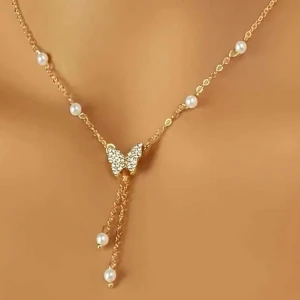 Guldhalsband med fjäril och pärlor - Säljer ett elegant guldhalsband med en vacker fjärilsdetalj i mitten. Halsbandet har små pärlor jämnt fördelade längs kedjan och två hängande kedjor med pärlor i slutet. Råkade beställa dubbletter ☺️