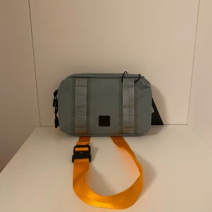 DB Axel Väska  - DB Axel Väska i färg grön och axelremmen orange. Ny pris 1400 kr.