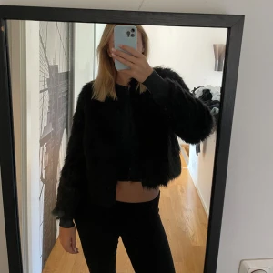 Svart pälsjacka - Säljer en supersnygg svart pälsjacka. Den är perfekt för att hålla sig varm och stilren nu till hösten/ vintern! Jackan har en normal passform och långa ärmar, vilket gör den både bekväm och trendig.