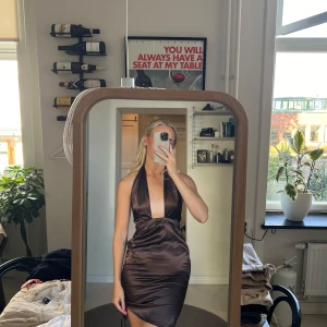 Svart halterneck klänning - Säljer en elegant svart halterneck klänning med öppen rygg. Klänningen är i ett glansigt material som ger en lyxig känsla. Perfekt för festliga tillfällen!