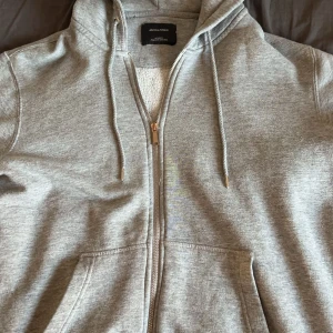 Grå hoodie från Jack & Jones - Säljer en grå hoodie från Jack & Jones i storlek M. Den har en dragkedja framtill och en mysig fleecefodrad insida. priset är ej hugget i sten.