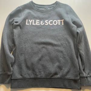 Grå tröja från Lyle & Scott - Säljer en snygg och bekväm grå tröja från Lyle & Scott. Den har en klassisk design med långärmade ärmar och en rund halsringning. Perfekt för både vardag och skola