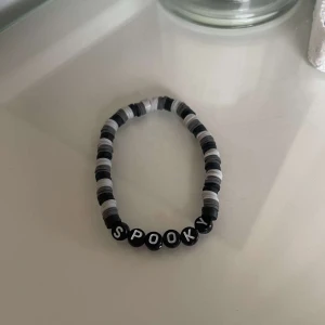 Svart och vitt armband med texten SPOOKY - Säljer ett coolt armband i svart och vitt med bokstäver som bildar ordet 'SPOOKY'. Perfekt för Halloween eller när du vill ha en lite mystisk stil. Armbandet är elastiskt och passar de flesta handleder.