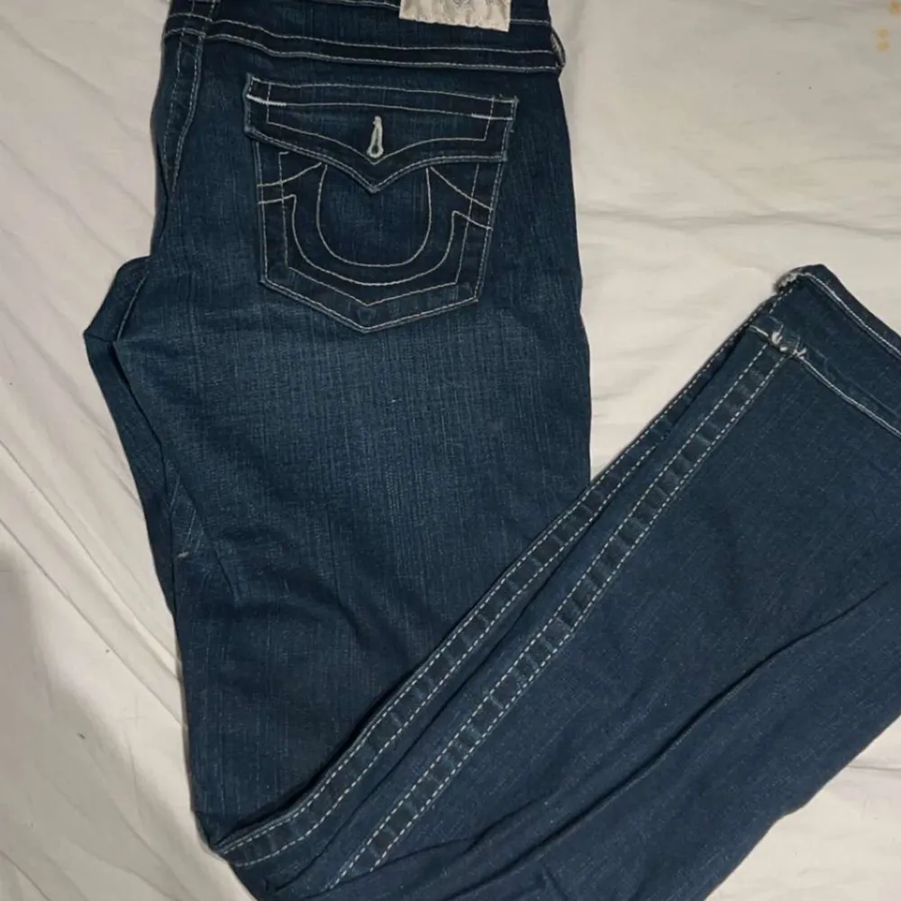 Säljer ett par snygga mörkblå jeans från True Religion. De har en klassisk femficksdesign med coola bakfickor som har vita sömmar och knappar. Jeansen är i bra skick och perfekta för både vardag och fest. Passar dig som gillar en stilren look!. Jeans & Byxor.