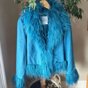 Blå jacka med fuskpäls från Bershka - Säljer en supercool blå jacka från Bershka med fuskpälsdetaljer. Jackan har en fluffig krage och ärmar med päls, vilket ger den en unik look. Perfekt för att sticka ut i mängden! Den är i bra skick och passar perfekt för höst och vår.🩵💙🩵