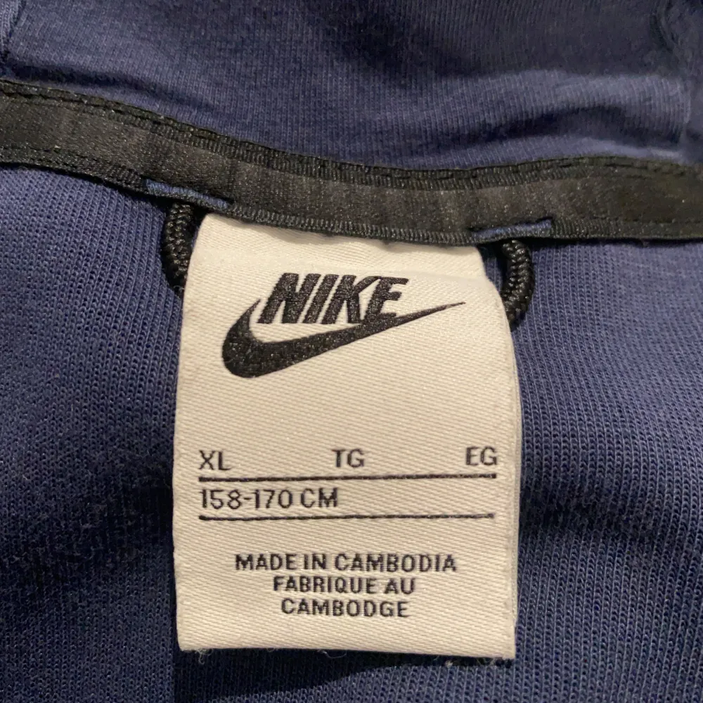 Säljer en snygg blå Nike tech fleece från Nike i storlek (158-170 cm). Den har en dragkedja framtill och en praktisk ficka på ärmen. Perfekt för kyliga dagar eller som en extra lager under jackan. Hoodien är i bra skick och redo för nya äventyr!. Takit.