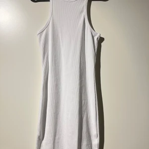 Vit ribbad klänning från Gina Tricot - Säljer en superfin vit ribbad klänning från Gina Tricot. Den är ärmlös och har en tight passform som är perfekt för sommardagar. Klänningen är aldrig använd och passar både till vardags och fest. Perfekt att styla med sneakers eller sandaler!
