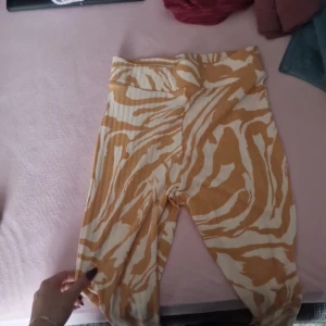 Gula och vita mönstrade leggings från H&M - Säljer ett par supercoola leggings från H&M i storlek XS. De har ett snyggt gult och vitt mönster som påminner om zebra. Perfekta för att liva upp vilken outfit som helst! De är stretchiga och bekväma, idealiska för både vardag och fest.