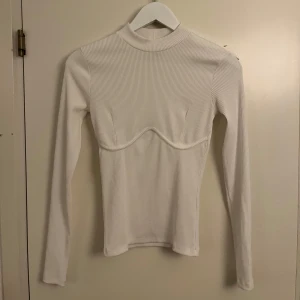 Ribbad halvpolo  - Vit ribbad halvpolo med detalj under brösten. Använd 2 gånger, så väldigt fint skick. Storlek XS från Nelly.