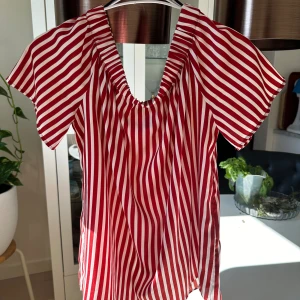 Röd- och vitrandig offshoulder-topp - Säljer en superfin röd- och vitrandig offshoulder-topp. Den har korta ärmar och en luftig passform, perfekt för sommardagar. Toppen är gjord i ett lätt och bekvämt material.