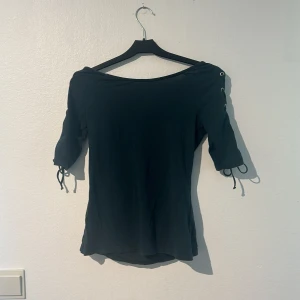 Svart topp med snörning - Säljer en grön off shoulder topp med halvlånga ärmar och snygg snörning längs sidorna. Toppen är tight och passar bra till både vardag och fest. Den är i fint skick då den inte varit använd någon gång!💕