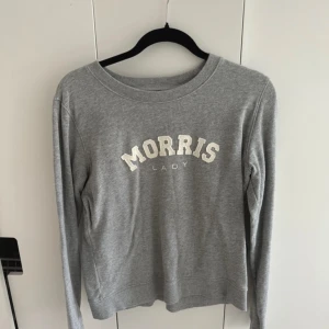Grå tröja från Morris Lady - Säljer en snygg och bekväm grå tröja från Morris. Den har ett stilrent tryck med texten 'Morris Lady' på framsidan. Tröjan är långärmad och perfekt för en avslappnad stil. Passar bra till både jeans och kjol!