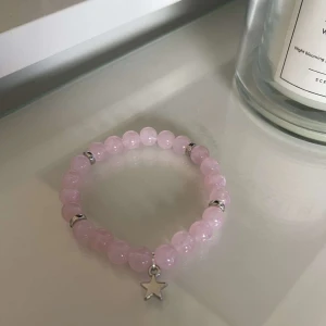 Rosa pärlarmband med stjärnhänge - Säljer ett supergulligt rosa pärlarmband med ett litet stjärnhänge. Armbandet har silverfärgade detaljer mellan pärlorna som ger det en extra touch. Perfekt för att piffa upp vilken outfit som helst!