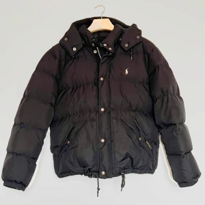 Ralph Lauren Dunjacka - Säljer en snygg och högkvalitativ dunjacka från Ralph Lauren i svart färg. Perfekt för kyliga dagar då den både är stilren och otroligt varm tack vare sitt dunfyllda material. Hör av er vid intresse 📌  ✔ Värmande & lätt - dunfyllning ger maximal värme utan att kännas tung ✔ Hög kvalitet - klassiskt Ralph Lauren-snitt med snygga detaljer ✔️ Material - 100% dun  Längd: 62cm | bredd 58cm