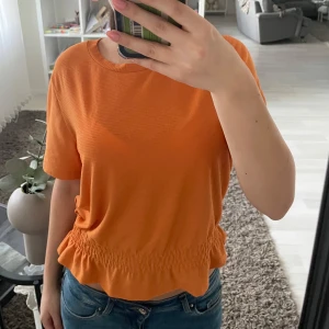 Orange topp från Gina Tricot - Säljer en snygg orange topp från Gina Tricot. Den har korta ärmar och en elastisk midja som ger en fin passform. Perfekt för en färgglad look!