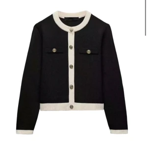 Svart och vit kofta med knappar - Snygg svart kofta med vita detaljer och knappar framtill. Den har långa ärmar och två dekorativa fickor på bröstet. Perfekt för en stilren look.