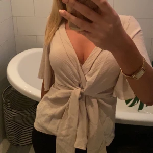 Beige omlottopp från Shein - Säljer en snygg beige omlottopp från Shein med korta vida ärmar och knytning framtill. Perfekt för en stilren look. Toppen är i ett lätt och luftigt material. Säljer då den inte kommer till användning❤️