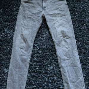 Grå jeansbyxor från Lee - Säljer ett par grå jeansbyxor från Lee i modellen Rider. Byxorna har en klassisk femficksdesign och är tillverkade i ett slitstarkt material. Perfekta för en avslappnad stil. Slim fit.
