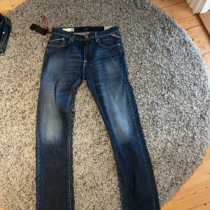 Blå jeans från Replay - Säljer ett par snygga blå jeans från Replay, modell Mini Waitom. De har en klassisk femficksdesign med knapp och dragkedja. Jeansen har en regular fit och är tillverkade av återvunnet material för en hållbar stil.