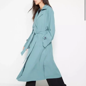 Blå trenchcoat från Lindex - Snygg blå trenchcoat från Lindex i storlek XS. Storleken är mer som M. Jackan har ett klassiskt snitt med knappar och ett bälte i midjan för en elegant look. Kan också användas som klänning💙Nypris 799kr